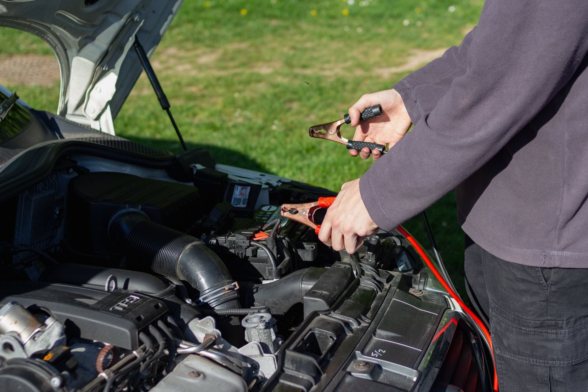 Mechanik na zewnątrz podłącza kable rozruchowe do akumulatora auta