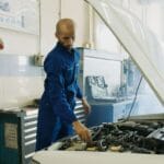 Mechanik w niebieskim kombinezonie sprawdza silnik samochodu w warsztacie