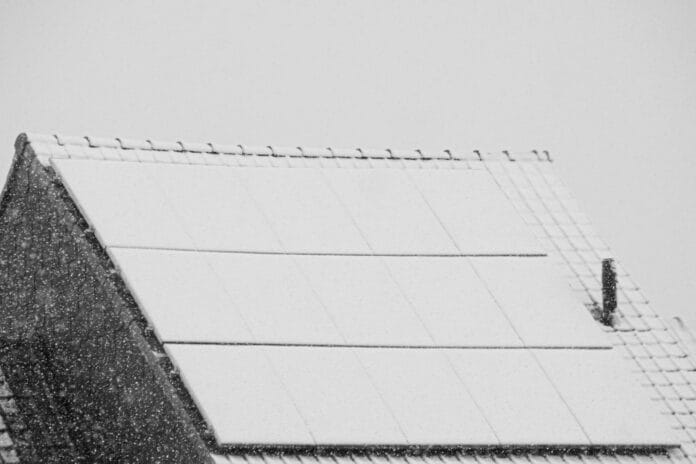 Ośnieżone panele fotowoltaiczne na dachu zimą jako symbol wyzwań OZE
