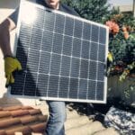 Technik niesie panel fotowoltaiczny na dachu podczas montażu instalacji PV